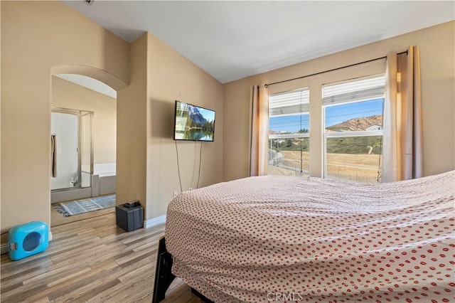 bedroom featuring lofted ceiling, wood finished floors, arched walkways, and connected bathroom