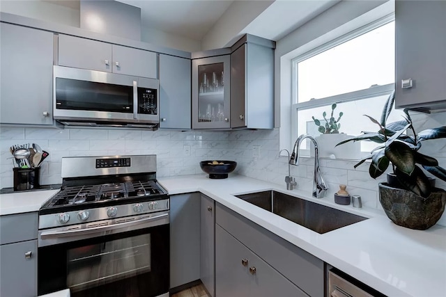 2151 S W View St, Los Angeles, CA 90016 - kitchen featuring stainless steel appliances, gray cabinetry, light countertops, tasteful backsplash, and glass insert cabinets