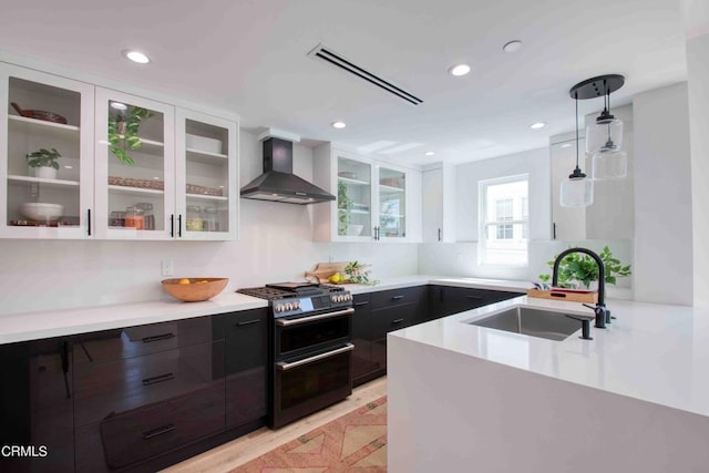 kitchen featuring double oven range, white cabinets, sink, wall chimney exhaust hood, and decorative light fixtures