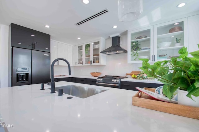 kitchen featuring white cabinets, wall chimney exhaust hood, high end refrigerator, black range with gas stovetop, and sink