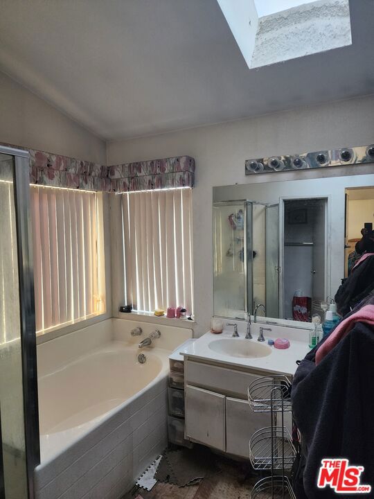 bathroom featuring lofted ceiling with skylight, shower with separate bathtub, and vanity