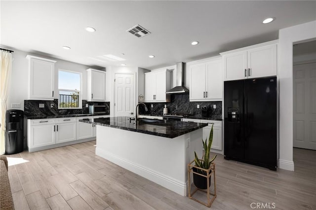 kitchen with white cabinets, light hardwood / wood-style flooring, black refrigerator with ice dispenser, and wall chimney range hood