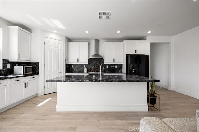 kitchen featuring black fridge, wall chimney range hood, and a kitchen island with sink