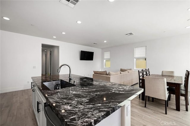 kitchen with dishwasher, light hardwood / wood-style floors, dark stone countertops, and sink