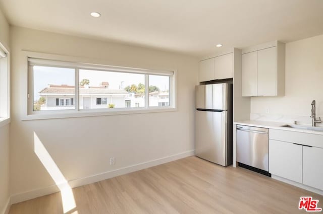 kitchen with appliances with stainless steel finishes, sink, white cabinetry, and light hardwood / wood-style floors