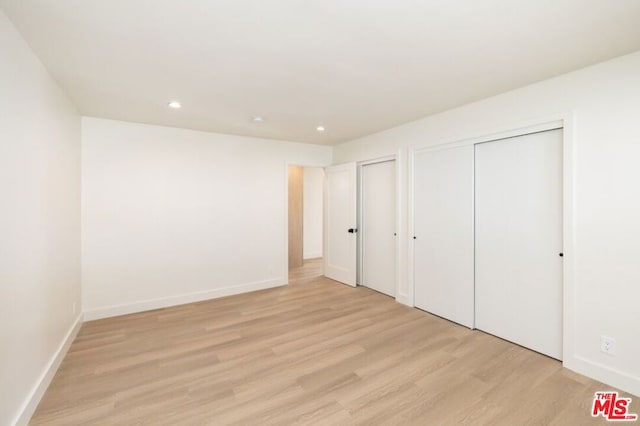 unfurnished bedroom with multiple closets and light hardwood / wood-style floors