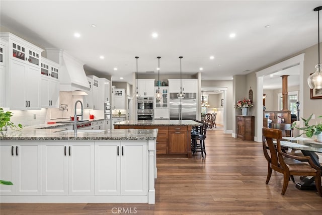 kitchen with a sink, a peninsula, dark wood finished floors, stainless steel appliances, and custom range hood