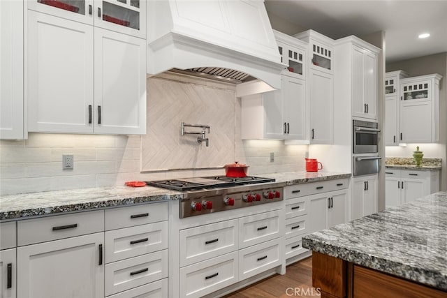 kitchen featuring white cabinets, custom exhaust hood, light stone countertops, appliances with stainless steel finishes, and a warming drawer