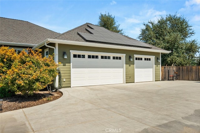 garage featuring roof mounted solar panels, driveway, and fence