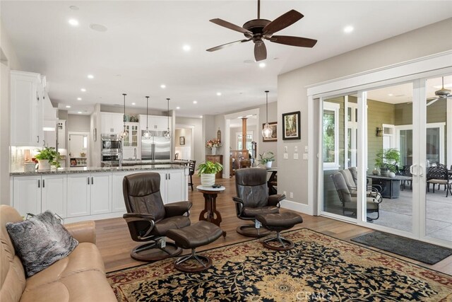living room featuring a ceiling fan, baseboards, light wood-style flooring, and recessed lighting