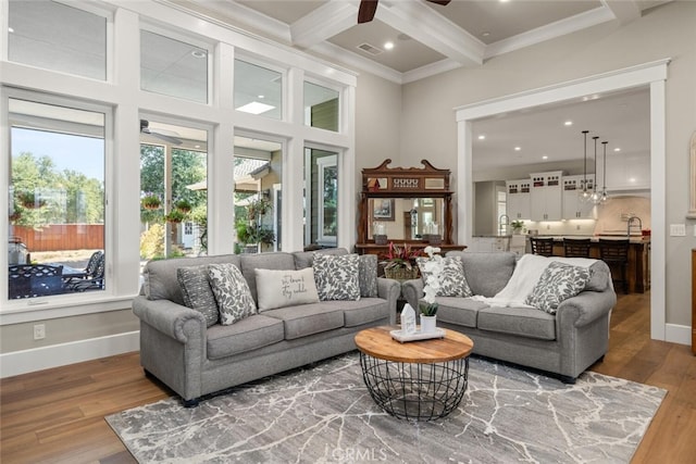 living room featuring ornamental molding, wood finished floors, a ceiling fan, beam ceiling, and coffered ceiling