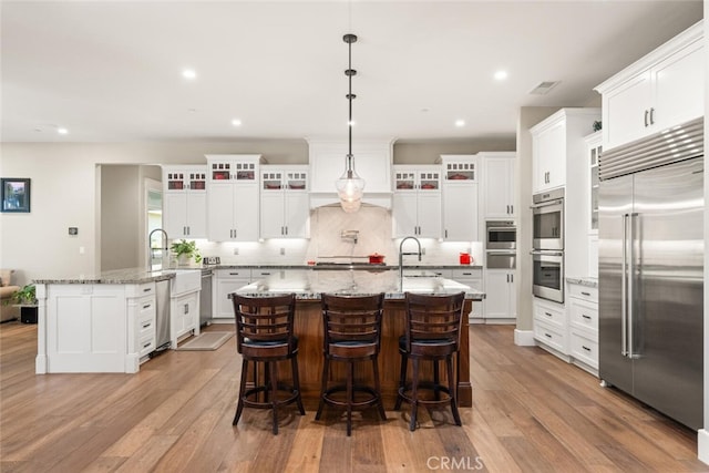 kitchen featuring a center island with sink, decorative backsplash, light hardwood / wood-style flooring, and stainless steel appliances