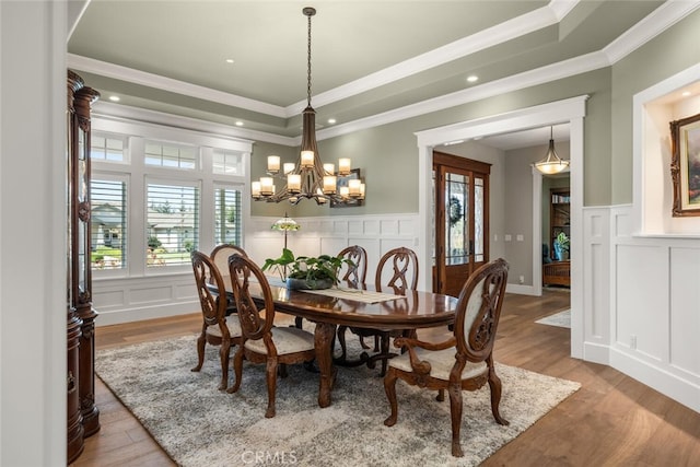 dining space with hardwood / wood-style flooring, a raised ceiling, ornamental molding, and an inviting chandelier