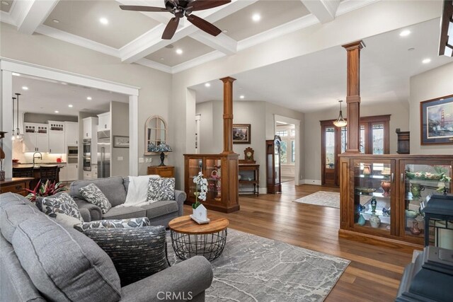living area featuring ornate columns, wood finished floors, a ceiling fan, and beam ceiling