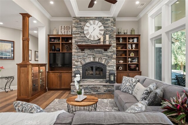 living room with ceiling fan, wood-type flooring, a stone fireplace, and ornamental molding