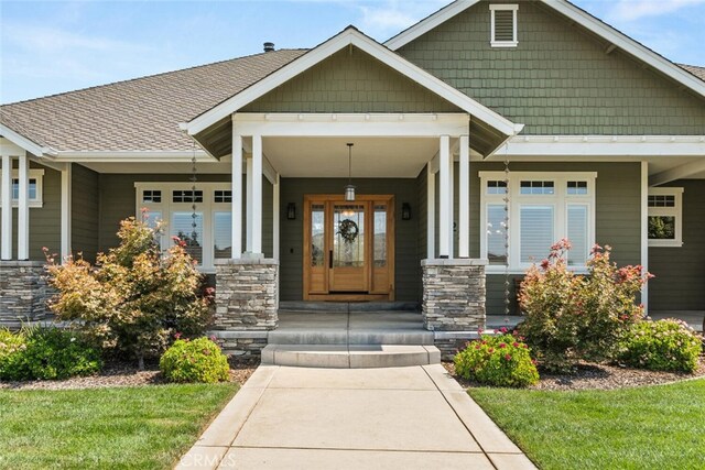 entrance to property with stone siding, a shingled roof, and covered porch