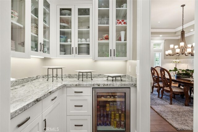 bar featuring beverage cooler, pendant lighting, wood-type flooring, white cabinetry, and an inviting chandelier