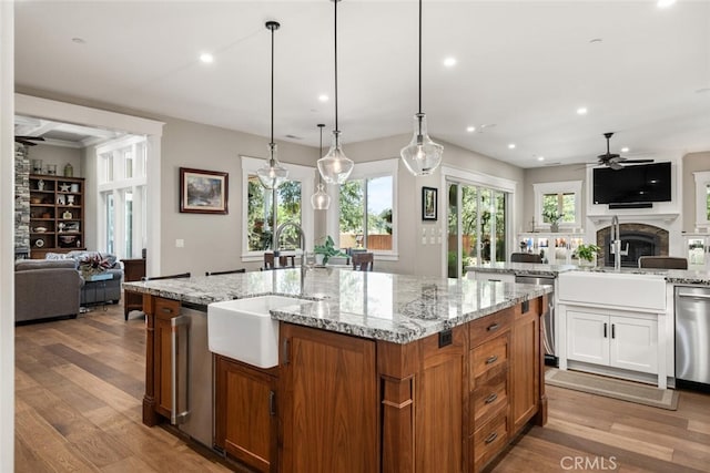 kitchen featuring ceiling fan, an island with sink, a sink, open floor plan, and stainless steel dishwasher