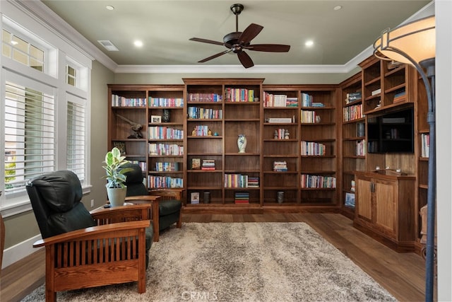 sitting room with a ceiling fan, wood finished floors, baseboards, visible vents, and ornamental molding