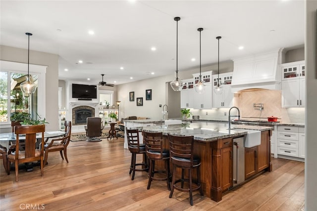 kitchen with backsplash, a ceiling fan, light wood finished floors, a large island, and custom range hood