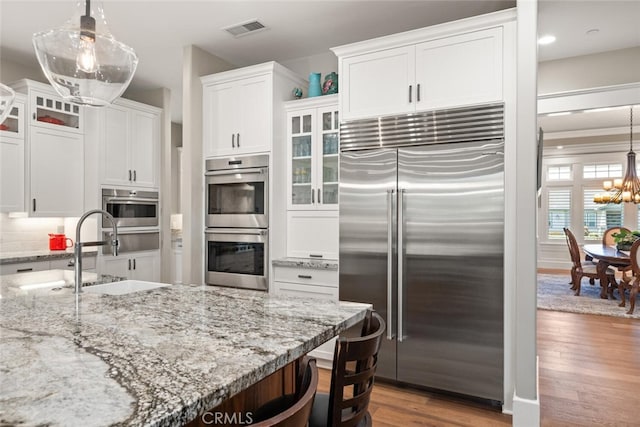 kitchen with stainless steel appliances, backsplash, hardwood / wood-style flooring, white cabinets, and decorative light fixtures