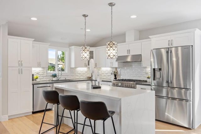 kitchen featuring appliances with stainless steel finishes, white cabinetry, sink, hanging light fixtures, and a center island