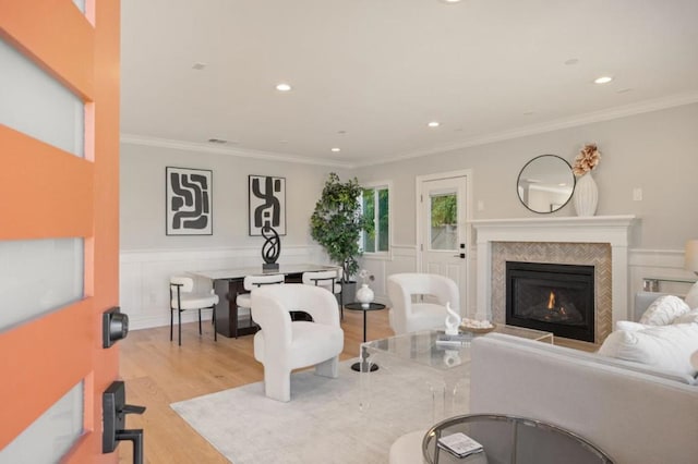 living room with a tiled fireplace, ornamental molding, and light hardwood / wood-style floors