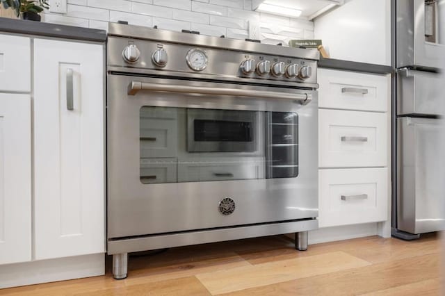 kitchen featuring high end stainless steel range oven, white cabinetry, tasteful backsplash, and light hardwood / wood-style floors