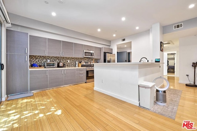 kitchen featuring a breakfast bar, light hardwood / wood-style floors, backsplash, and appliances with stainless steel finishes