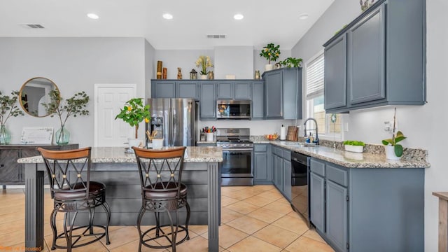 kitchen featuring sink, a breakfast bar area, a kitchen island, stainless steel appliances, and light stone countertops