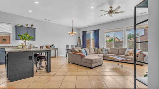 tiled living room with ceiling fan with notable chandelier