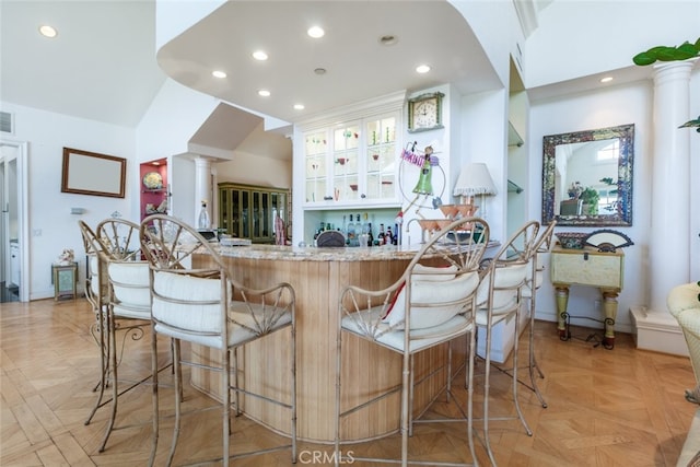 kitchen with a breakfast bar, light stone counters, light parquet flooring, white cabinets, and kitchen peninsula