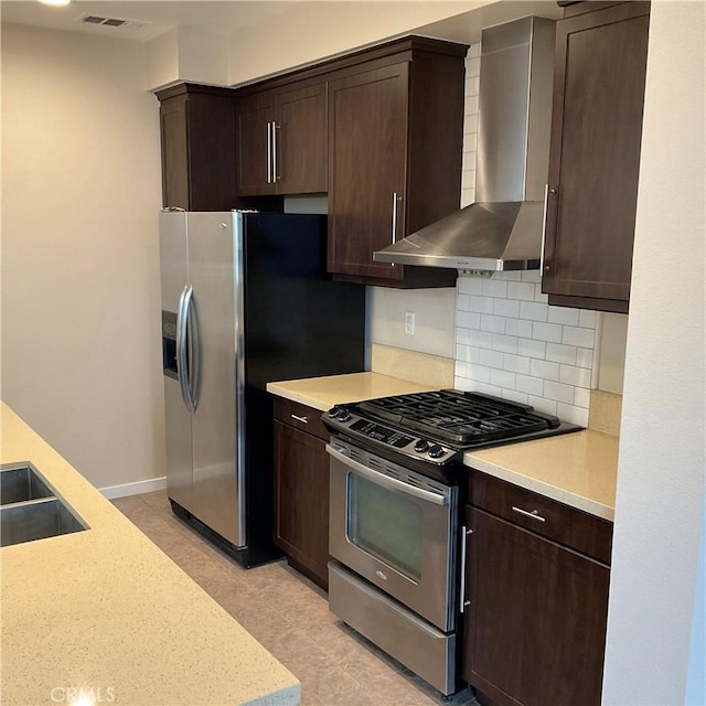 kitchen featuring stainless steel appliances, wall chimney exhaust hood, dark brown cabinets, and tasteful backsplash