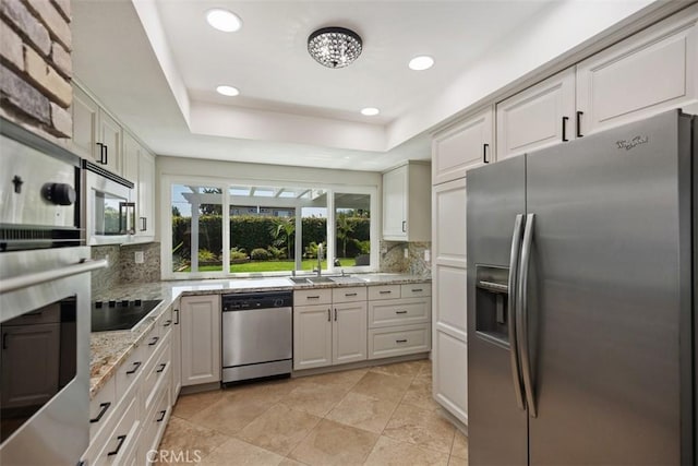 kitchen featuring backsplash, appliances with stainless steel finishes, a tray ceiling, and white cabinetry