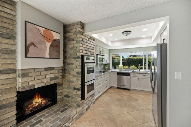 kitchen featuring a brick fireplace, sink, appliances with stainless steel finishes, a textured ceiling, and white cabinets