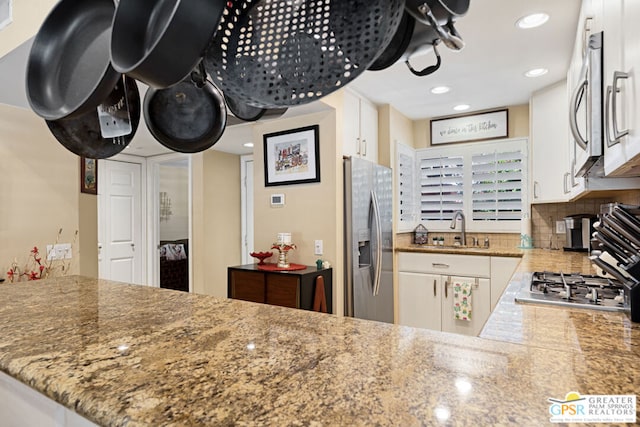 kitchen featuring kitchen peninsula, stainless steel appliances, white cabinetry, and sink