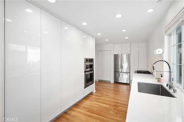 kitchen featuring sink, white cabinets, appliances with stainless steel finishes, and light hardwood / wood-style floors