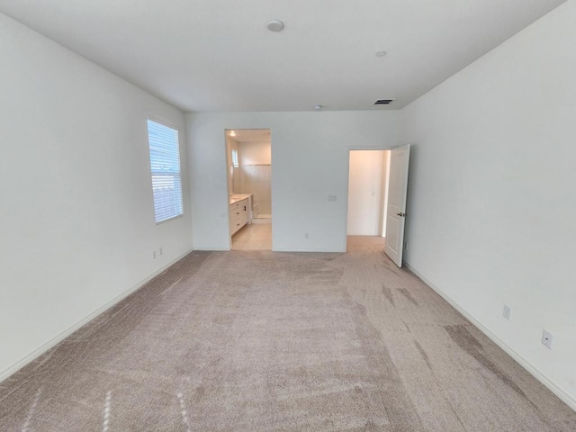 unfurnished bedroom featuring light colored carpet and ensuite bath