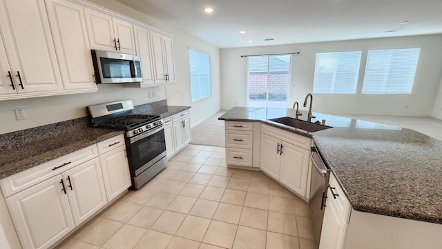 kitchen with sink, light tile patterned floors, dark stone countertops, white cabinets, and appliances with stainless steel finishes