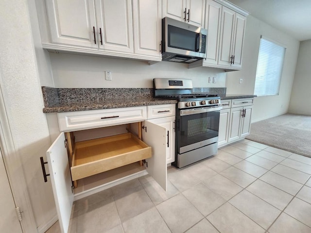 kitchen with light tile patterned flooring, dark stone countertops, white cabinetry, and stainless steel appliances