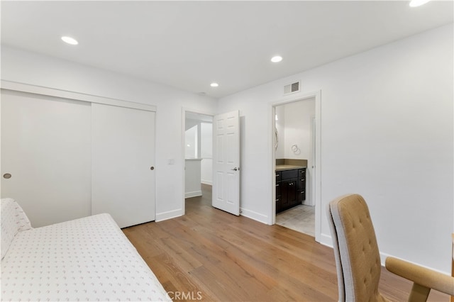 bedroom featuring ensuite bath, light wood-type flooring, and a closet