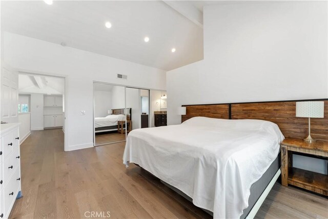 bedroom featuring lofted ceiling with beams, a closet, and light hardwood / wood-style floors