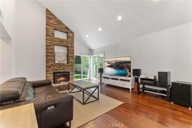 living room with high vaulted ceiling, a stone fireplace, and dark wood-type flooring