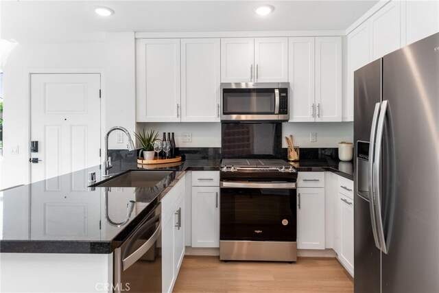 kitchen featuring light wood finished floors, white cabinets, a peninsula, stainless steel appliances, and a sink