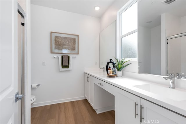 full bath featuring double vanity, toilet, a sink, wood finished floors, and baseboards