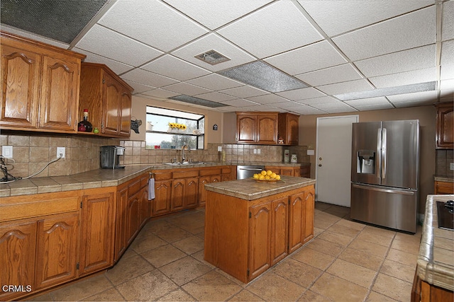 kitchen with light tile patterned floors, appliances with stainless steel finishes, a kitchen island, sink, and tasteful backsplash