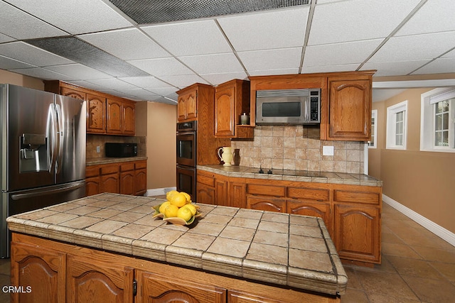 kitchen with dark tile patterned flooring, tasteful backsplash, black appliances, and tile counters