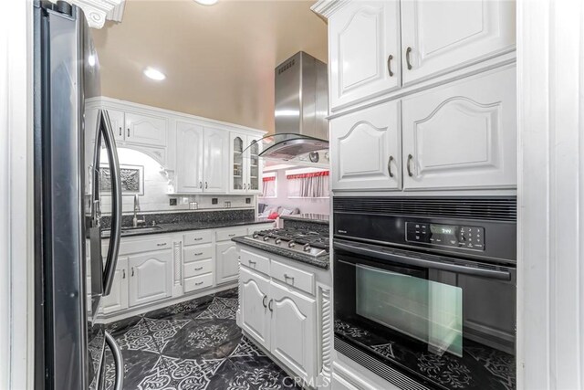 kitchen with refrigerator, black oven, dark tile patterned floors, wall chimney range hood, and stainless steel gas cooktop