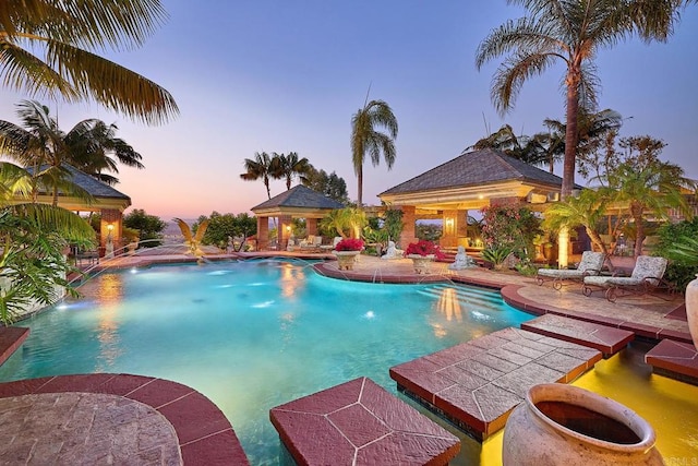 pool at dusk with pool water feature and a patio area