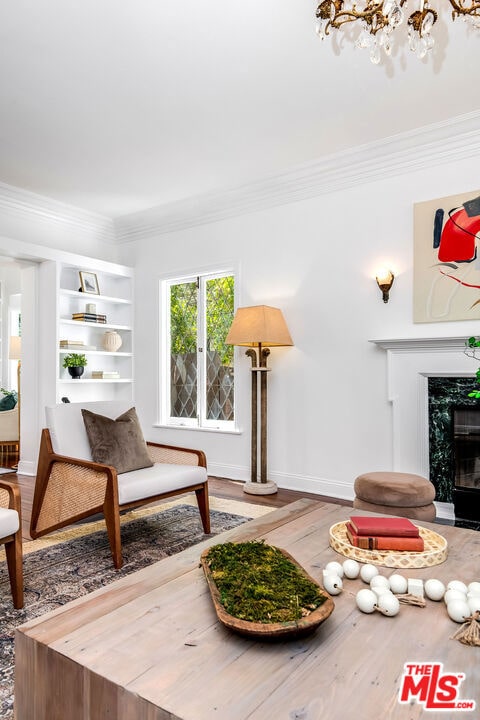 living room featuring hardwood / wood-style flooring, a high end fireplace, crown molding, and a notable chandelier